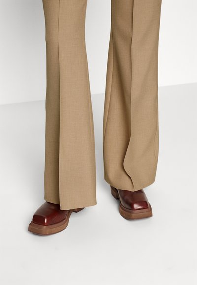 Pruunid laiad püksid siledast kangast, kombineeritud punaste läikivate nahast saapatega, millel on paks tald ja veidi ümar nina.