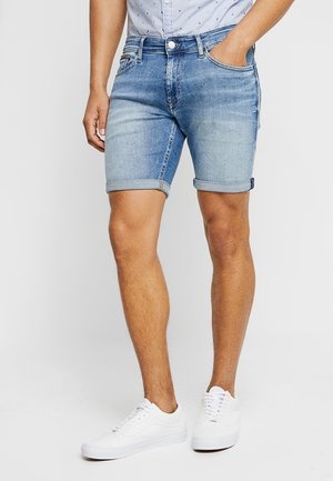 Shorts en denim bleu délavé avec ourlets retroussés, design à cinq poches et passants pour ceinture. Portés avec des baskets blanches, présentant une texture lisse et propre.