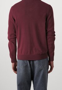 Burgundy tröja med ribbade muddar och nederkant, stickad textur, långa ärmar och en enkel design; bärs över grå, lösa jeans.