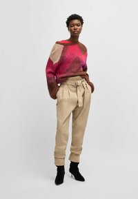 Strikket sweater i pink, creme og brun zigzag-mønster; parret med højtaljede beige bukser med bælte i taljen og sorte hæleboots.