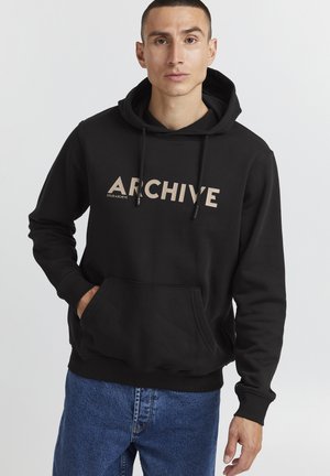 Sweatshirt à capuche noir avec poche kangourou, comportant le texte beige "ARCHIVE" sur le devant. Tissu doux, coupe décontractée, poignets côtelés.