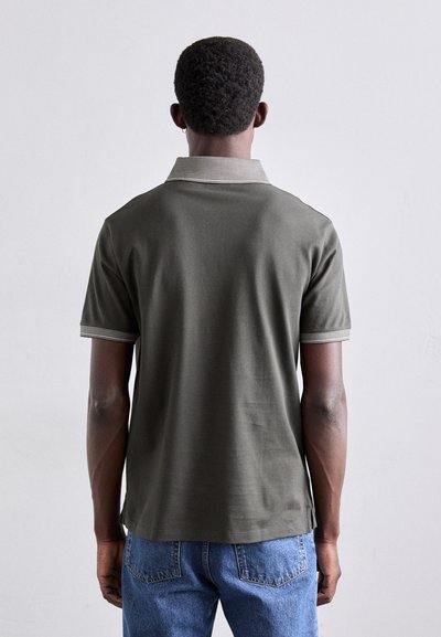 Olīvu zaļa polo krekls ar īsām piedurknēm, ar svītrainu apkakli un aprocēm. Audums izskatās gluds un viegls.