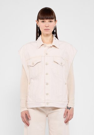 Light pink denim vest with a collared neck, oversized armholes, chest pockets, and snap buttons. Worn over a long-sleeve top.