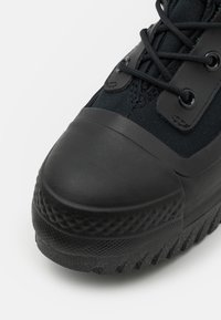 Schwarzer Sneaker mit einer strukturierten Gummizunge und einer dicken, gemusterten Sohle. Verfügt über ein Obermaterial aus Canvas und eine Schnürung mit Kunststoff-Ösen.