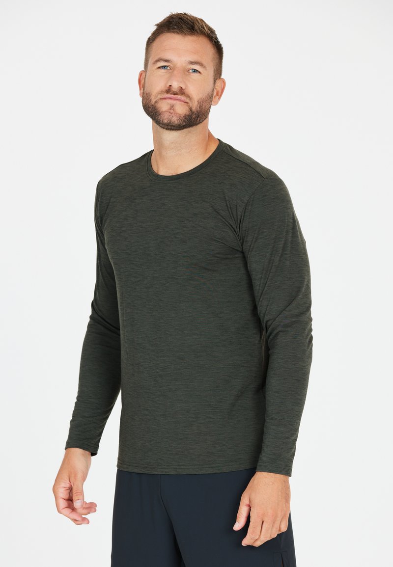 Musta vihreä pitkähihainen paita, jossa on teksturoitu kuvio, pyöreä kaula-aukko ja kapea leikkaus, yhdistettynä tummansinisiin urheiluhaalareihin.