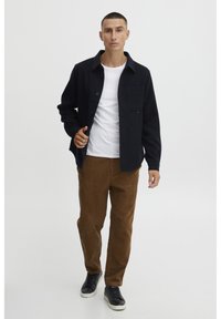 Navy button-up jacket over a white T-shirt, paired with brown corduroy pants and black sneakers. Simple design and textured materials.