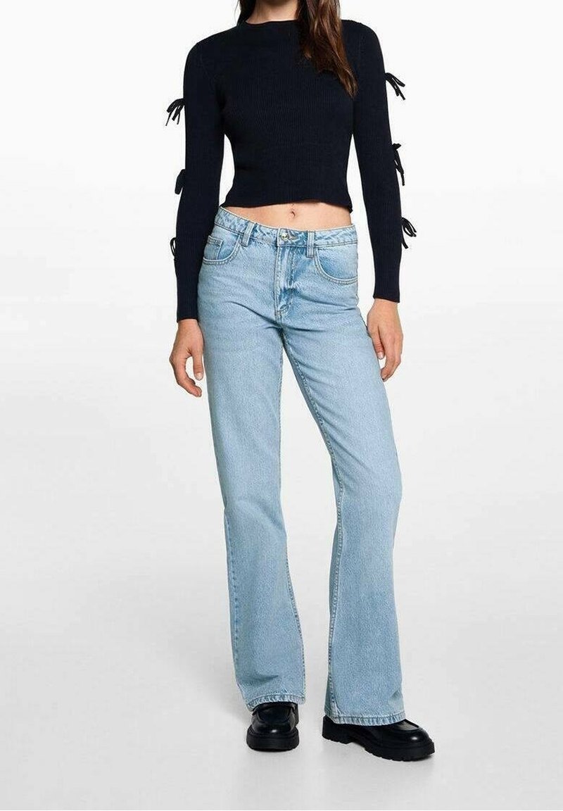 Pull noir tricoté court avec des accents de liens sur les manches, associé à un jean évasé bleu clair et des bottes épaisses noires.