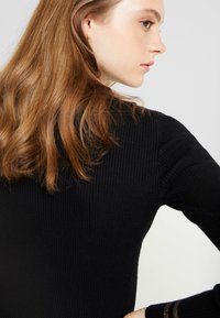 Schwarzes, geripptes Strickoberteil mit langen Ärmeln, einer taillierten Silhouette und dezenten goldenen Akzentstreifen an den Bündchen.