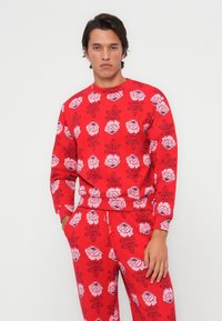Felpa rossa con un motivo floreale ripetuto in rosa, con contorni neri. Stile rilassato e polsini a costine.