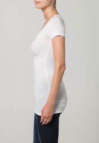 Bijela kratka majica s kratkim rukavima, slim fit kroja i V-izrezom, napravljena od glatkog materijala, uvučena u tamnoplave traperice.