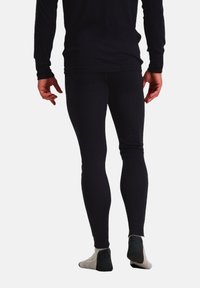 Zwarte thermoleggings met een gladde textuur, een aansluitend ontwerp en een hoge taille, gecombineerd met grijs en zwarte gemusterde sokken.