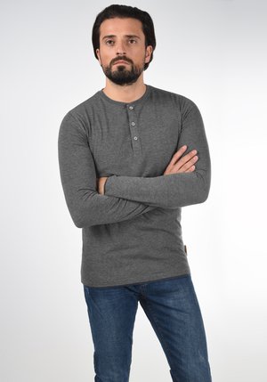 Camisa henley de manga larga en gris con tapeta de tres botones, hecha de tejido suave; combinada con jeans de mezclilla azul, que tienen un corte ajustado.