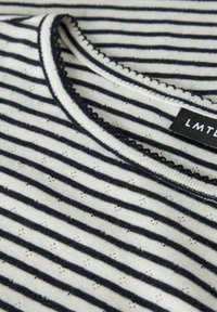 Top de manga corta a rayas en blanco y marino, con un escote redondeado con bordado de encaje, tejido texturizado y pequeños patrones de ojales en toda la prenda.