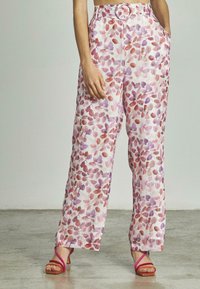 Pantalons larges fleuris en rose clair, présentant des motifs de feuilles rouges et violettes, une ceinture avec boucle ronde et des poches latérales.