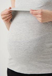 Siva, lagana, prilagodljiva majica napravljena od mekanog materijala, koja se lagano povlači kako bi otkrila zaobljeni srednji dio s suptilnom teksturom.