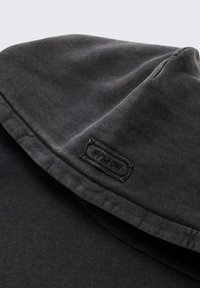 Donkergrijze hoodie met een textuurstof, zichtbare stitching en een klein, gestikt label op de halslijn.