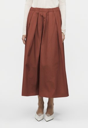 Γυναίκα που φοράει πλατιές παντελόνες culotte σε σκουριά απόχρωση, λευκό μπλουζάκι με μακριά μανίκια και λευκές μυτερές γόβες με λεπτομέρεια δαντέλας.