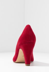 Scarpa con tacco alto in suede rosso, con punta affusolata, superficie liscia e tacco moderatamente curvo. La soletta interna presenta un marchio stampato.
