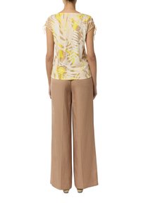 Kurzärmliges, beiges Oberteil mit gelbem und weißem tropischem Druck, kombiniert mit beigen weit geschnittenen Hosen, die über Zugbänder an den Ärmeln verfügen.