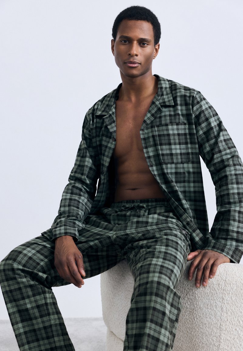 Green plaid pajama set made of soft fabric, featuring long sleeves, button-up shirt, and elastic waistband pants with a relaxed fit.
