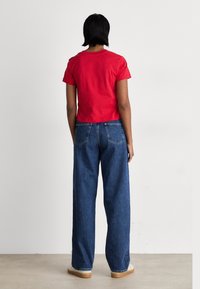 Maglietta rossa corta e jeans blu a vita alta con gamba larga. Vestibilità casual e texture morbida. Design semplice, senza motivi o loghi visibili.