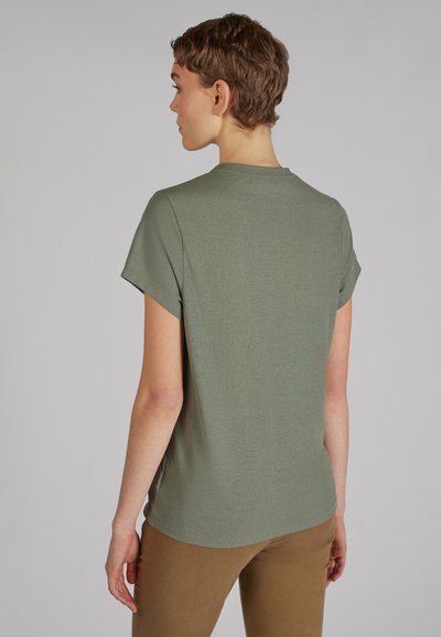 Oliwkowa koszulka z krótkim rękawem i okrągłym dekoltem o gładkiej teksturze, zestawiona z jasnobrązowymi dopasowanymi spodniami. Minimalistyczny design.