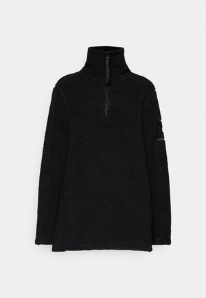 Black pullover fleece with a high collar and half-zip closure. Features textured fabric and a subtle patch detail on the sleeve.