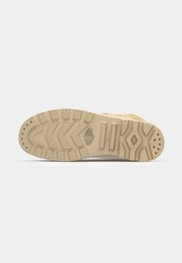 Semelle de sneaker beige en caoutchouc texturé, présentant un motif de bande de roulement en zigzag et des accents de grip circulaires. Comprend un marquage et des zones nervurées.