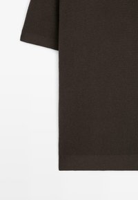 Maglione marrone a maniche corte lavorato a maglia con superficie strutturata e orlo a costine. Il tessuto presenta un motivo sottile che ne valorizza il design.