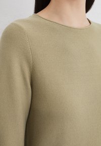 Olive green sweater with a textured knit, rounded neckline, and ribbed detailing at the edges. Close-up view of fabric and stitching.