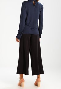 Marinblus med långa ärmar och ett nyckelhål på baksidan, ihopparad med vida svarta byxor, och har en mjuk textil och avslappnad passform.