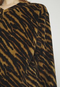 Tissu rayé tigre marron et noir sur un vêtement à manches longues porté par une personne, visible du cou au milieu du torse.