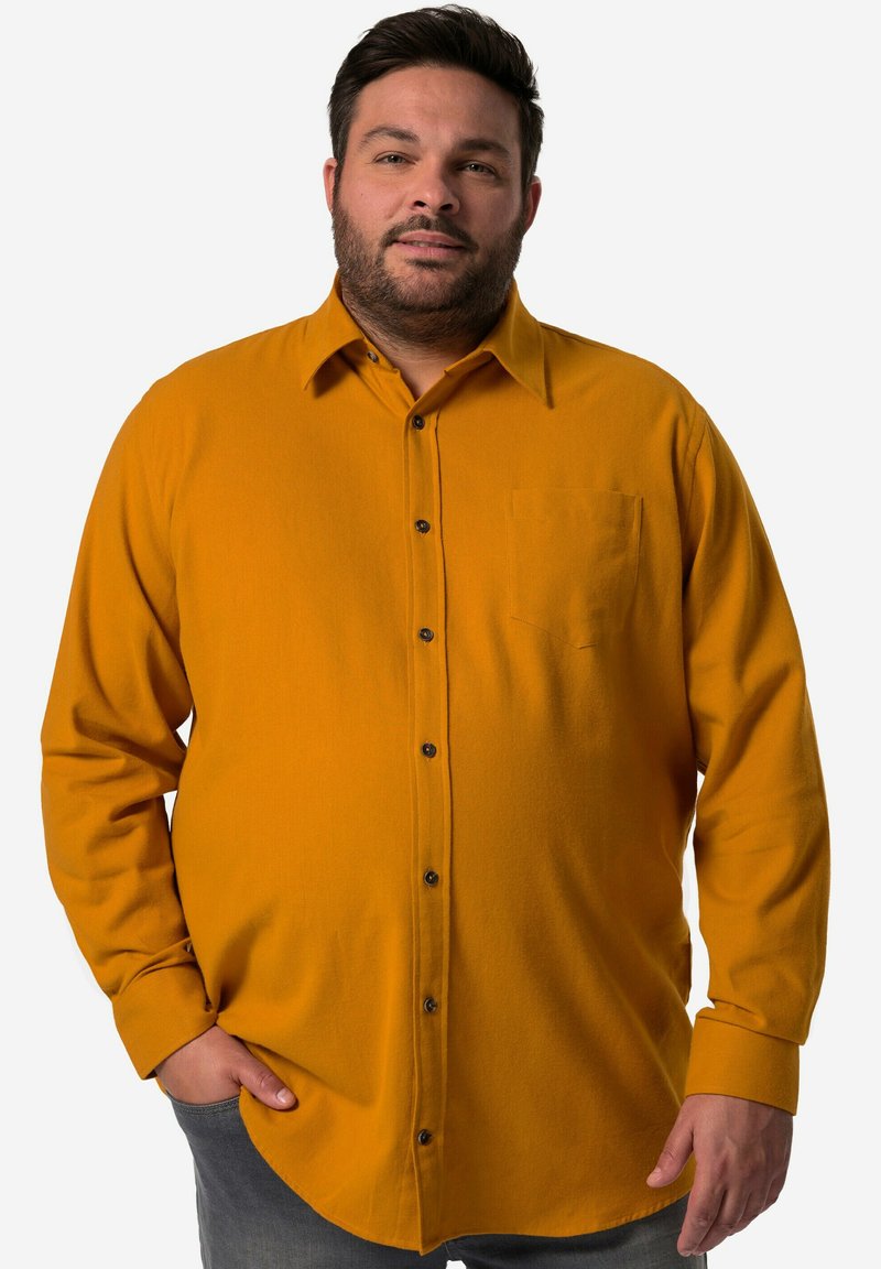 Camisa amarilla mostaza de botones en material suave, con un bolsillo y botones negros. Mangas largas con puños abotonados.
