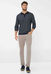 Pullover a maglia strutturata blu navy con colletto, abbinato a pantaloni slim-fit beige chiaro e sneaker blu scuro.
