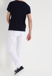 Navy blue short-sleeve t-shirt, white slim-fit jeans, and dark sneakers. The outfit features a relaxed fit and classic silhouettes.