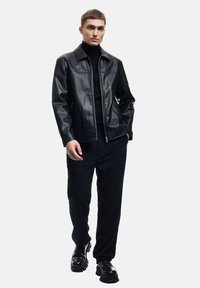 Sort læderjakke med lynlås, der har en klassisk krave, parret med en sort turtleneck, løse bukser og chunky sorte støvler.