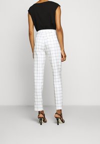 Pantalon blanc ajusté à motif quadrillé noir, taille haute et jambes fuselées. Associé à un haut noir à manches courtes et des escarpins à brides.