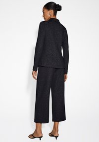 Completo a due pezzi nero e scintillante con giacca su misura e pantaloni a gamba larga. Tessuto morbido, design minimalista e dettagli di luccichio sottili.