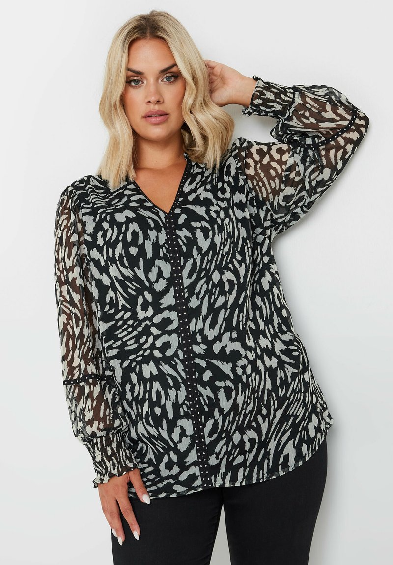 Blusa nera e grigia con motivo a righe, maniche a palloncino trasparenti, scollatura a V profonda e dettagli con bottoni sul davanti. Tessuto morbido e strutturato.