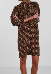 Kortärmad klänning i ett vågigt mönster av brunt, kräm och rost. Har hög halsringning och en lös passform, tillverkad av ett slätt tyg.