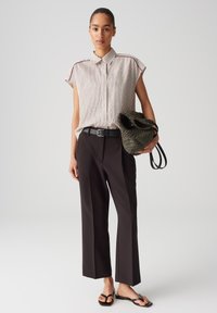 Striped short-sleeve shirt with collar, paired with high-waisted black trousers. Woven green bag with black straps, black flat sandals.