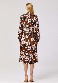 Robe midi à fleurs brune avec des manches longues, une taille ajustée et un ourlet fluide. Les fleurs sont de couleur rose et blanche, avec des accents noirs.