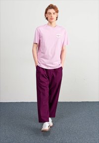 T-shirt di cotone rosa chiaro con una piccola grafica sul petto, abbinata a pantaloni larghi di colore viola scuro e scarpe da ginnastica bianche.