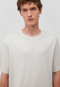 Hellgraues, oversized Herren T-Shirt aus Baumwolle mit rundem Halsausschnitt und kurzen Ärmeln, das eine glatte Textur und minimale Nahtdetails aufweist.