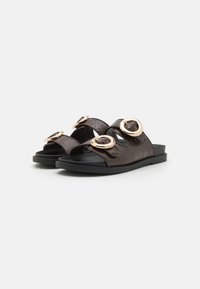 Brown quilted slide sandals with two large gold-tone circular accents, flat black sole, and open design for airflow.