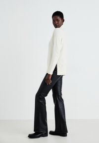 Cream sweater with a high neck and side slits, paired with black faux leather flared pants and chunky black boots. Simple, modern design.