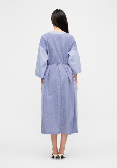 Ριγέ μπλε φόρεμα με σφιγμένη μέση, μανίκια τριών τετάρτων και κίτρινη κεντημένη ανθοδέσμη. Μήκος μέχρι τη μέση της γάμπας και κατασκευασμένο από βαμβακερό μείγμα υφάσματος.