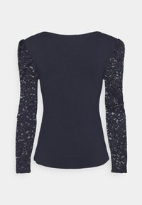 Haut noir cintré à manches longues avec manches en dentelle florale et col rond, présenté de dos sur fond blanc.