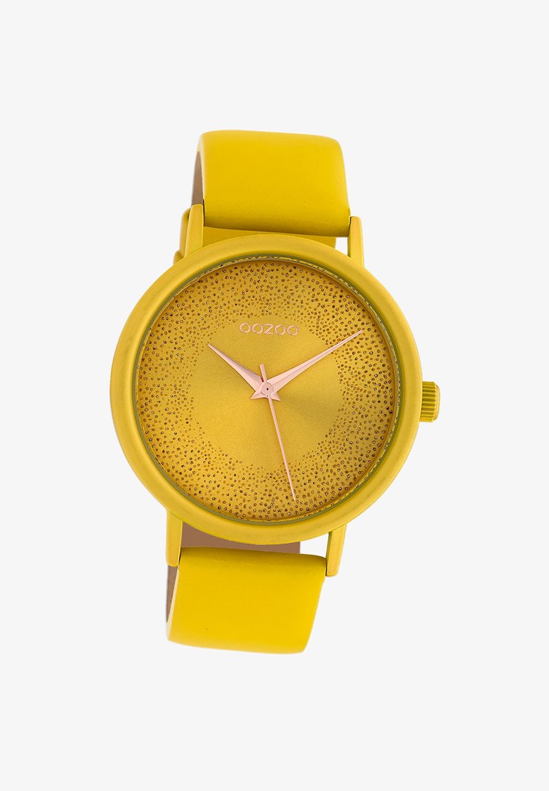 Montre avec un bracelet en silicone jaune et un boîtier rond assorti, un cadran texturé et des aiguilles en or rose. Elle présente un design minimaliste et moderne.