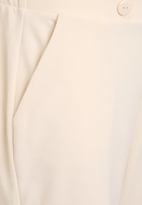Beige broeken met een gladde textuur, voorzien van een zijzak en een enkele knoopsluiting. Getailleerde pasvorm met subtiele plooien voor structuur.